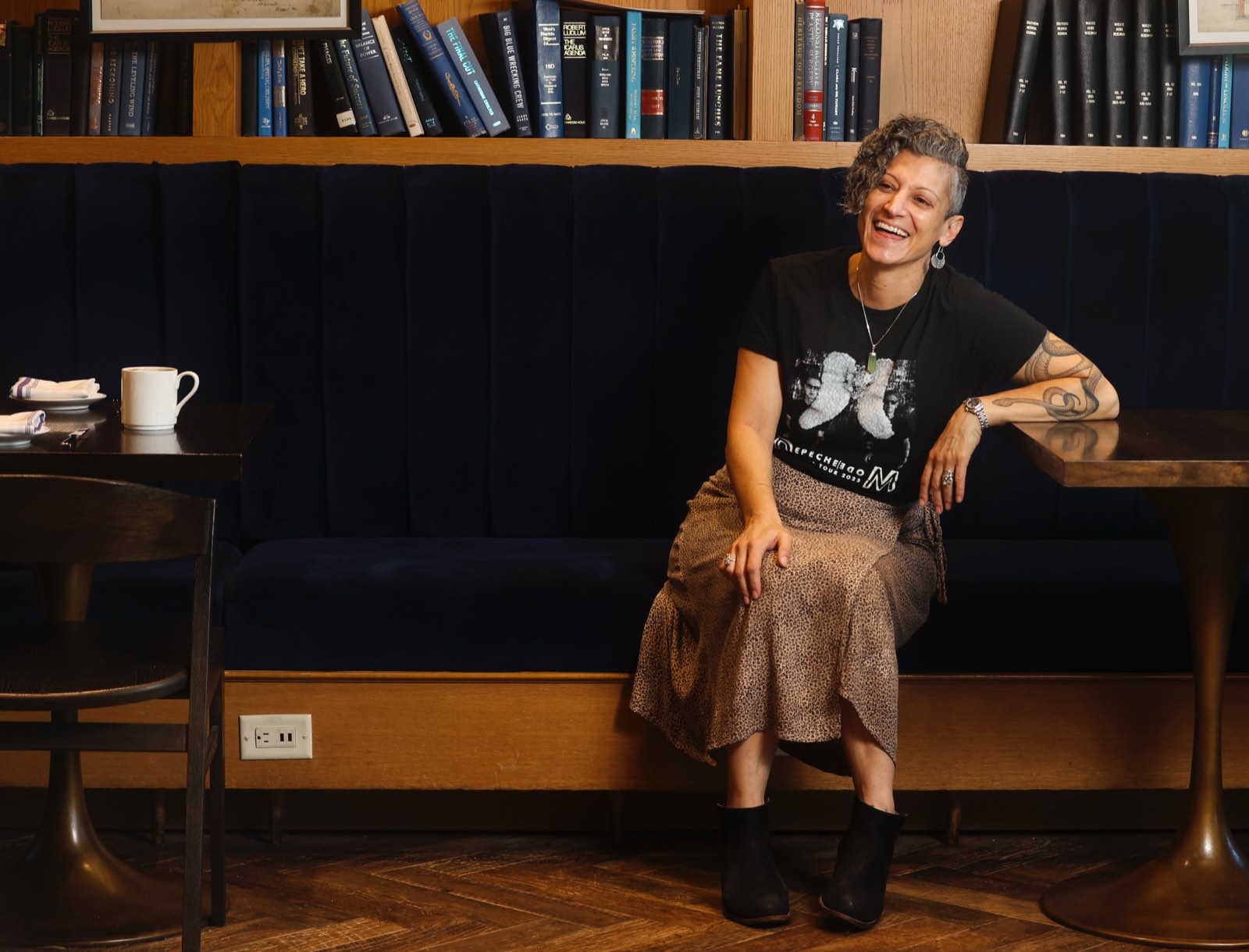 Emy Tafelski laughing on a navy velvet banquette in front of shelves of vintage books